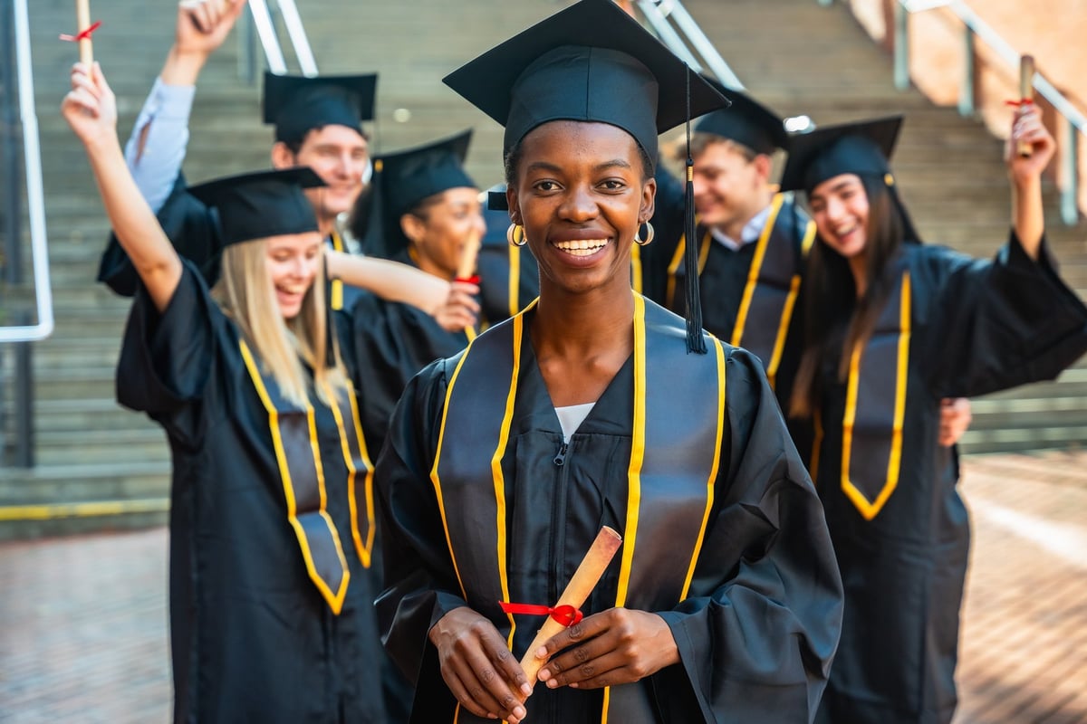 Diverse group of young adult graduates in caps and gowns smiling and holding diplomas